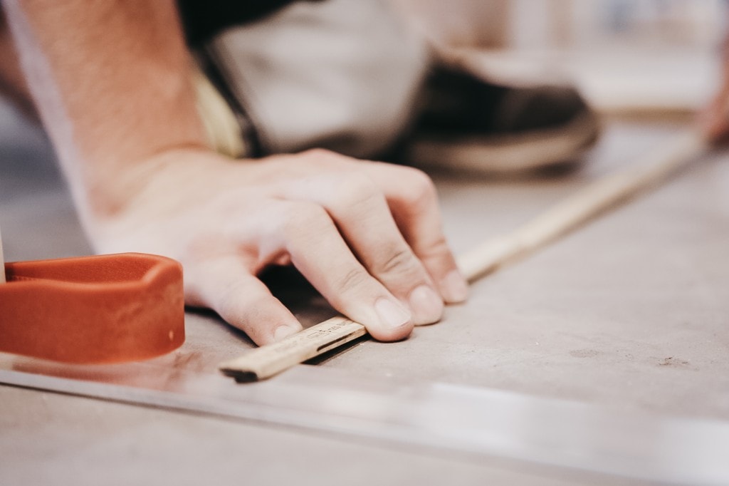 A pair of hands is using a ruler to measure the distances of aluminum columns of the AutoStore grid.