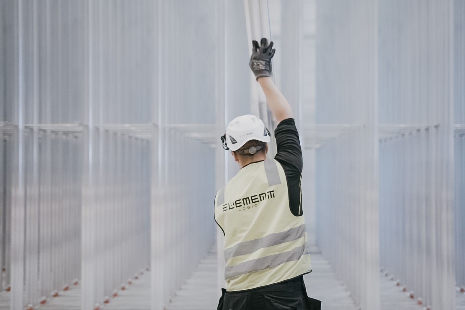 A man in a helmet and a yellow west is building the AutoStore grid consisting of aluminium columns.