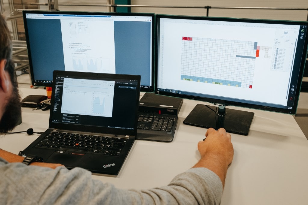 A man is working on the AutoStore solution with three computer screens.