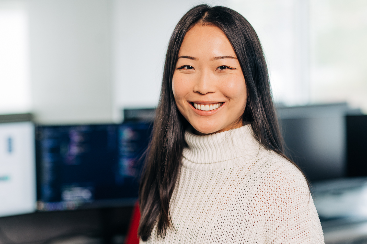 A woman is smiling in front of several computer screens.