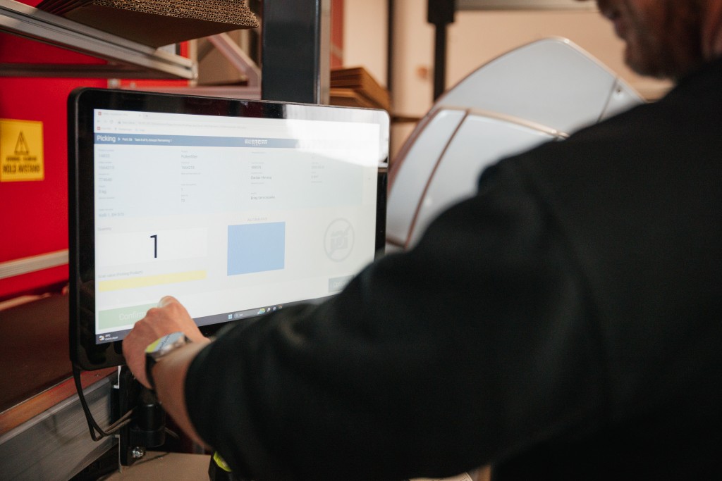 A man uses a touch screen to complete orders in an AutoStore system.