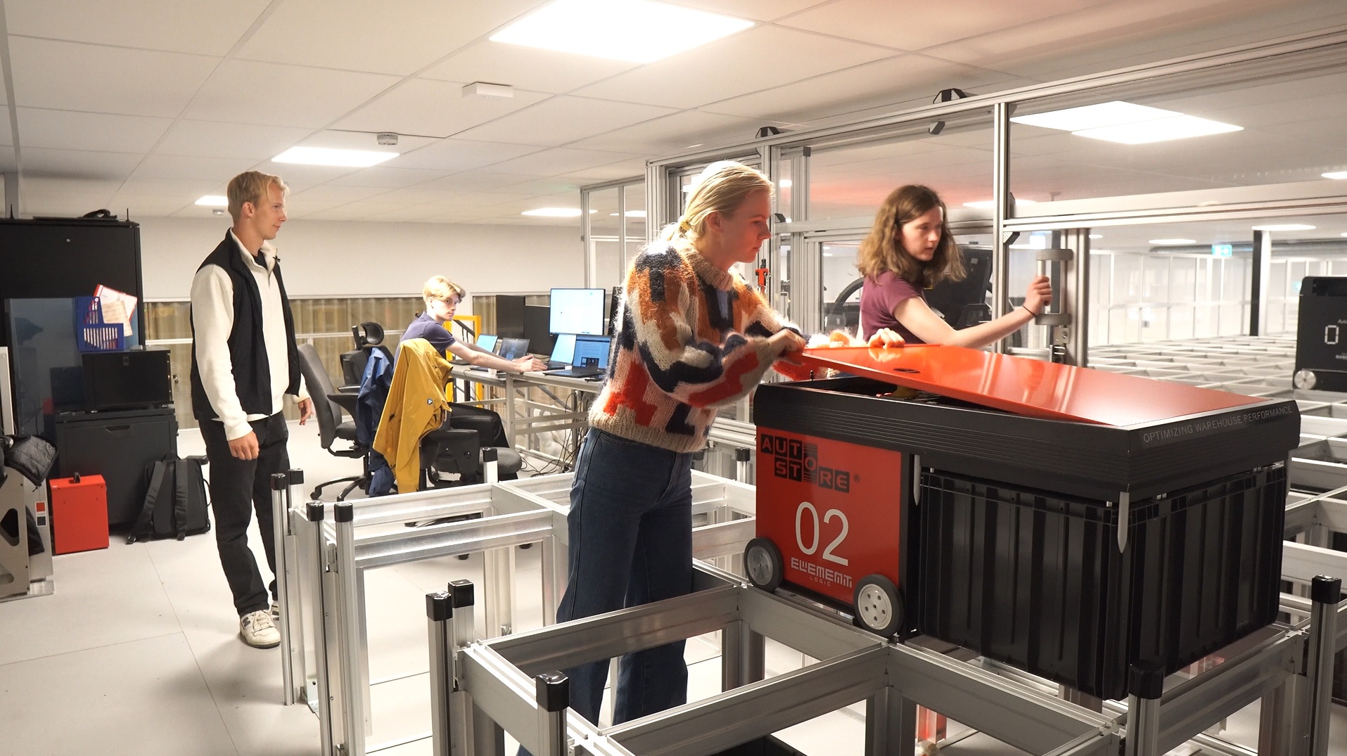 Student opening an AutoStore robot while another opens the hatch to the grid