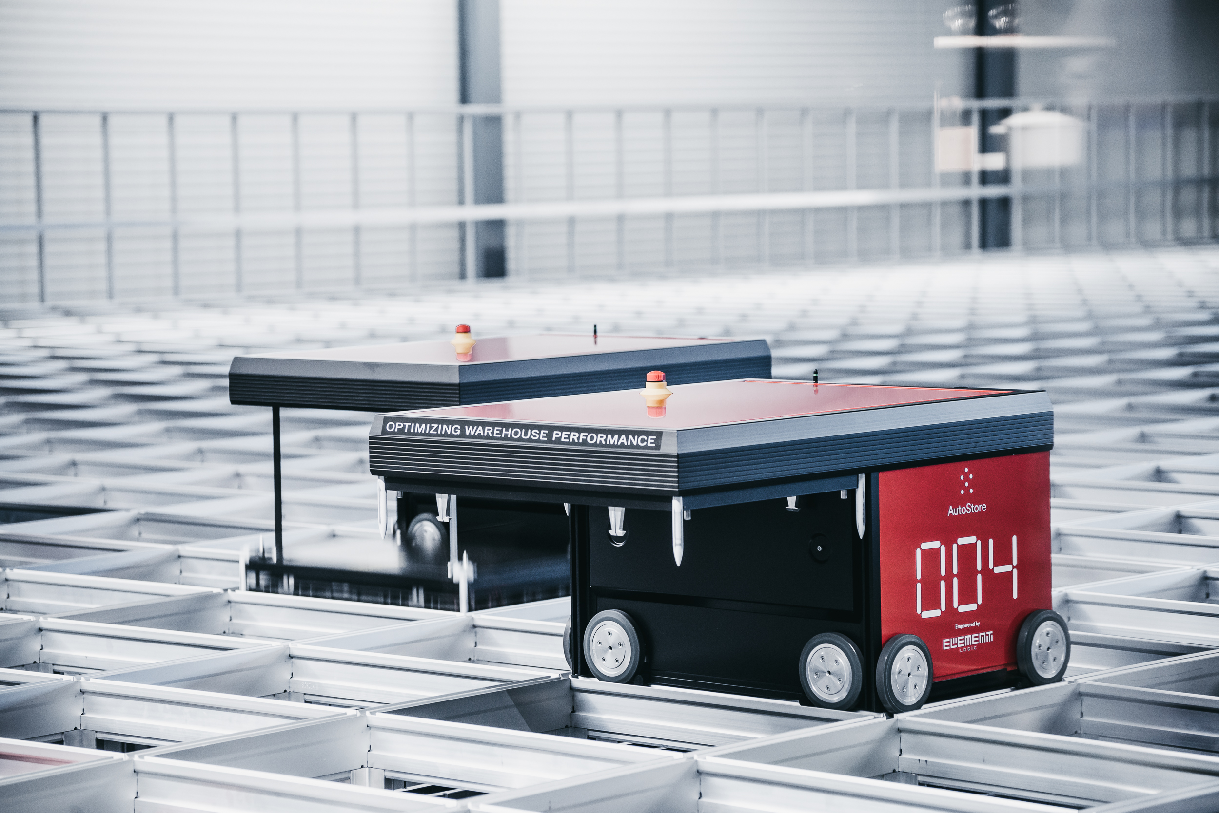 Two red AutoStore robots on top of an aluminum grid.