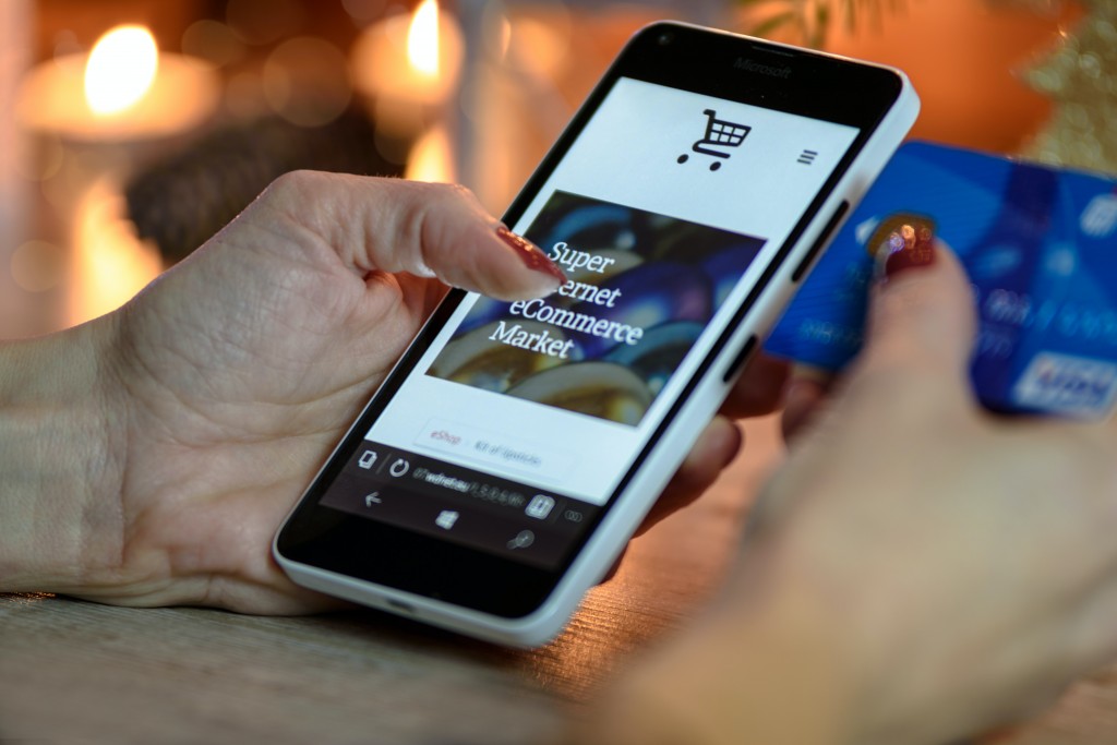 Hands holding a phone and bank card. The phone displays the text 'Super Internet e commerce market'