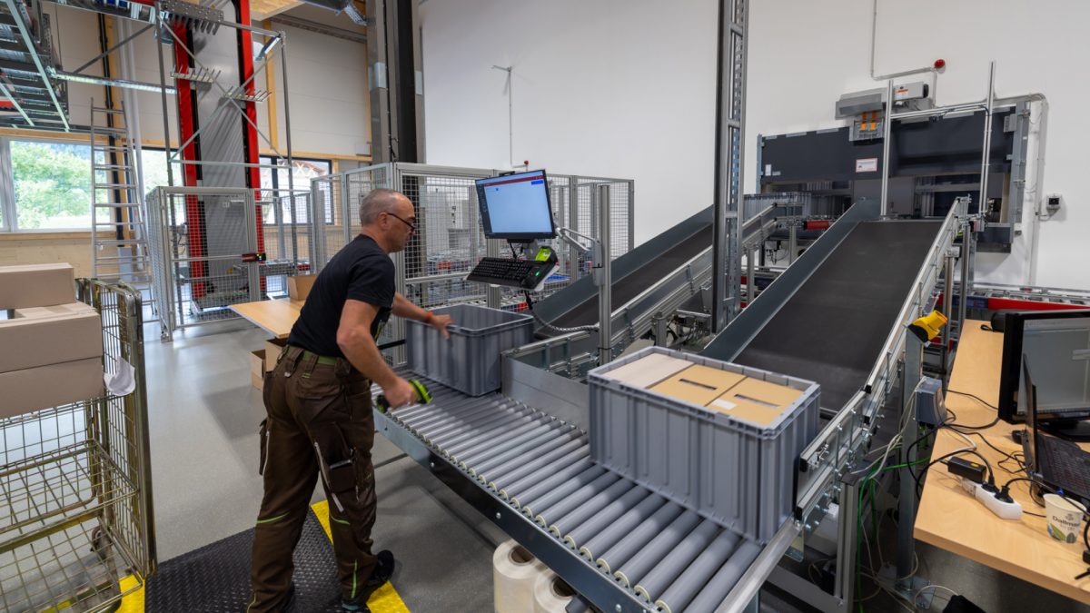 A man holding a bin by a conveyor belt