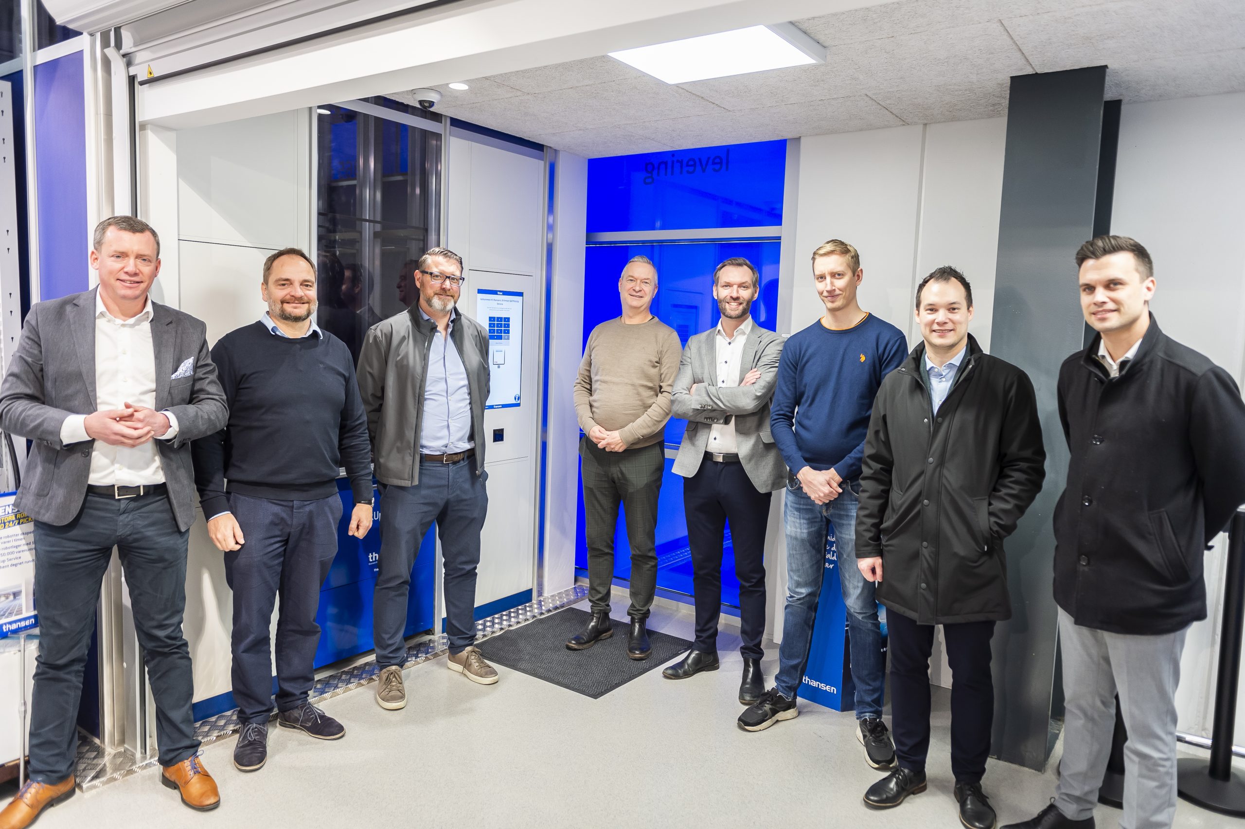 Eight men standing infront of an AutoStore port